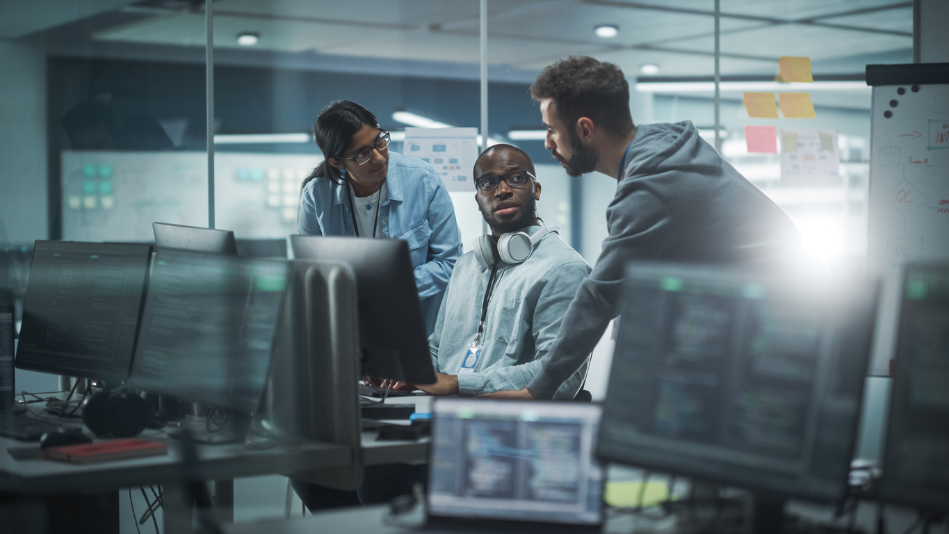 A Chief Information Security Officer Sits in Front of a Computer Talking to Two Colleagues.