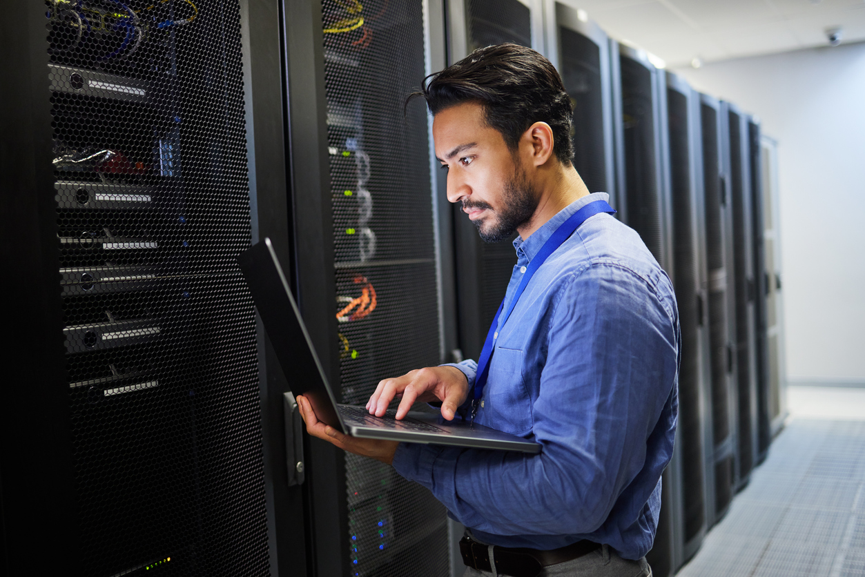 A Cybersecurity Expert Works on a Laptop While Standing in a Server Room.