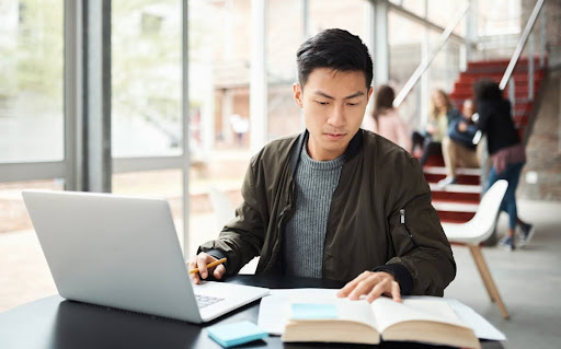 A student takes notes while conducting research using a laptop.