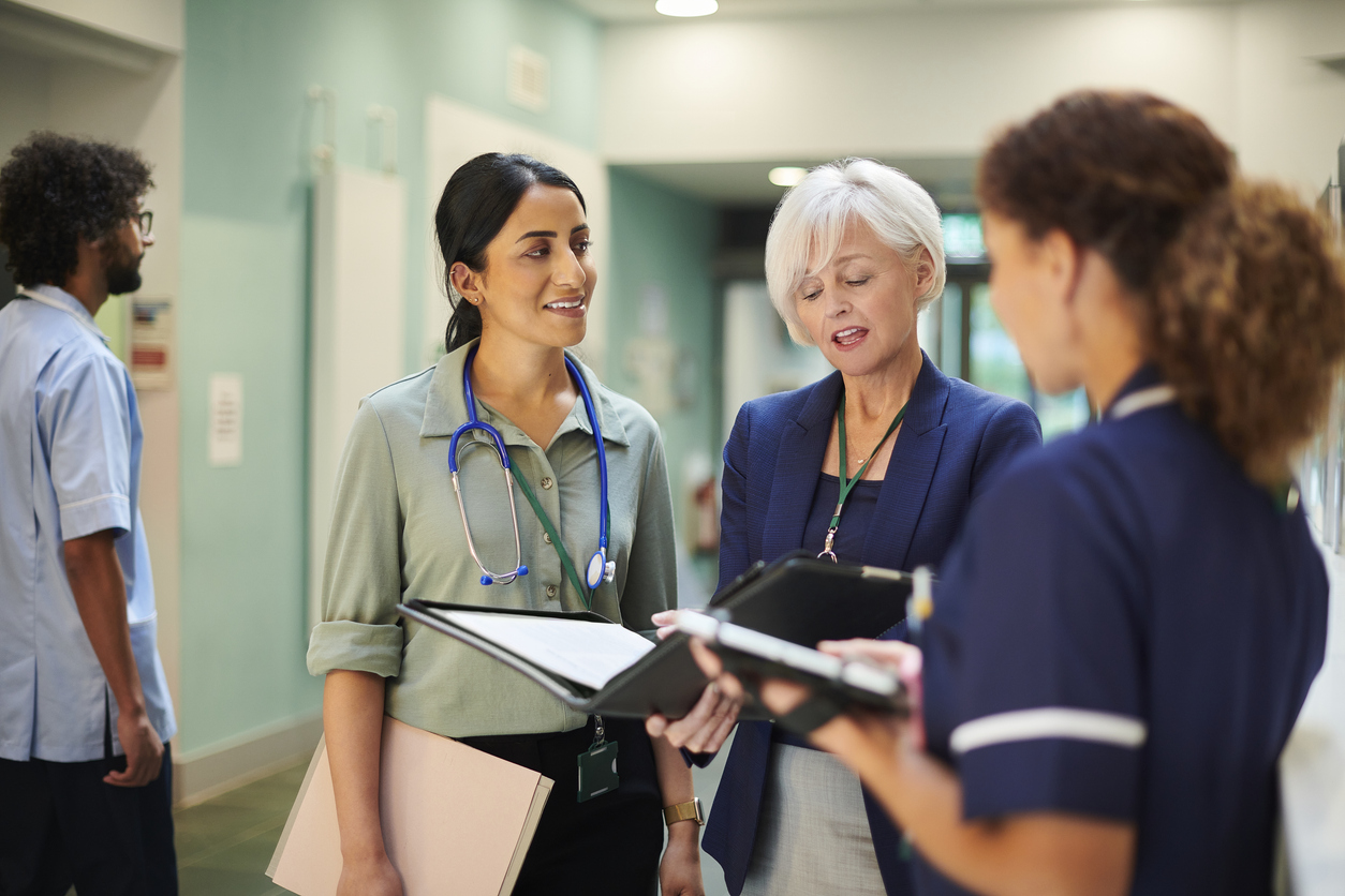 A Nurse Executive Talks With a Doctor and a Nurse in a Hospital Hallway.
