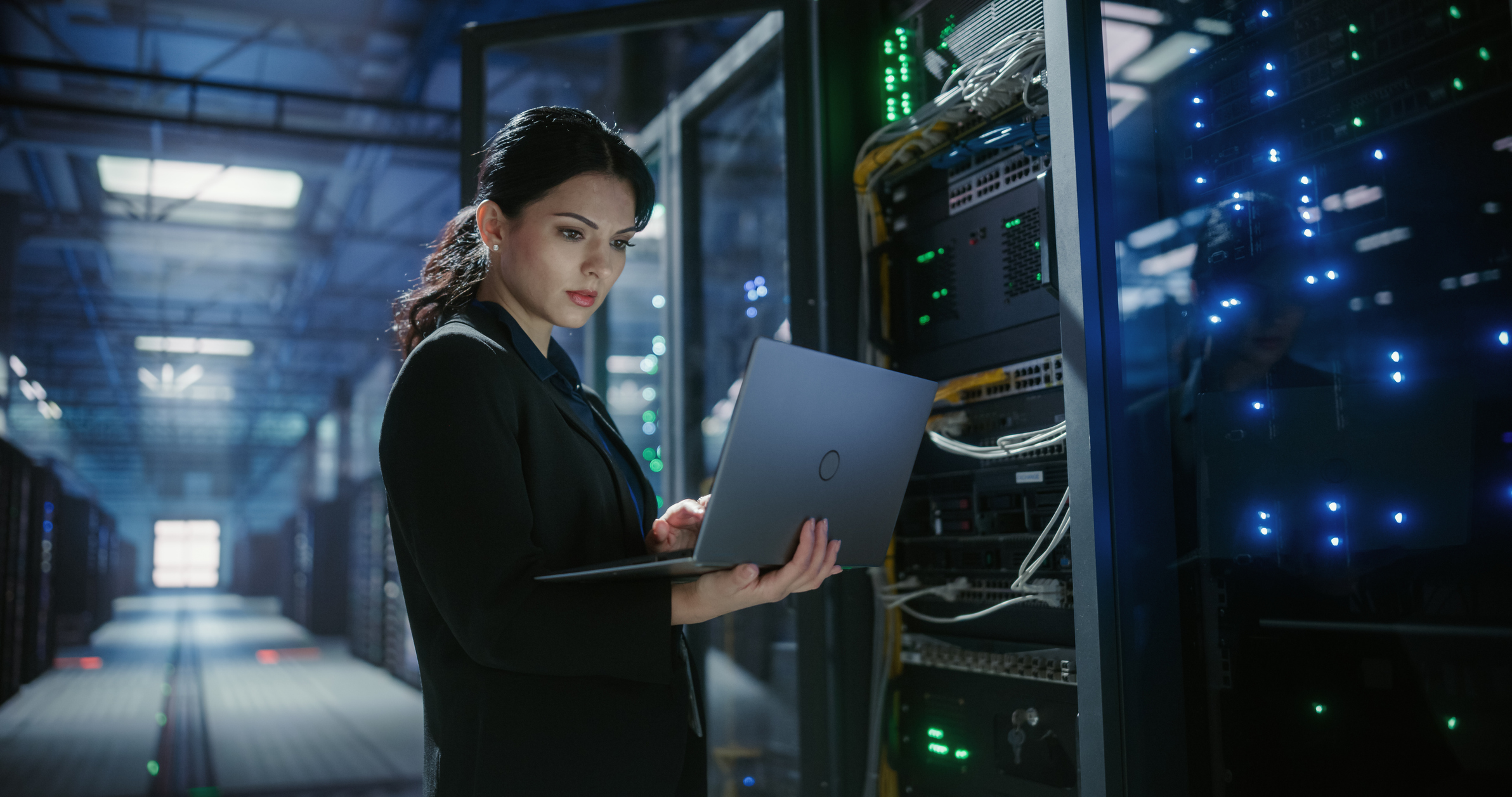 A cybersecurity professional in a server room uses a laptop to monitor network traffic.