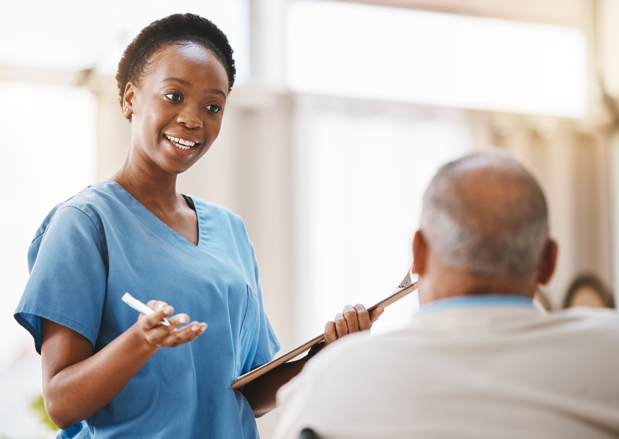Nurse holding a clipboard and talking to a patient.