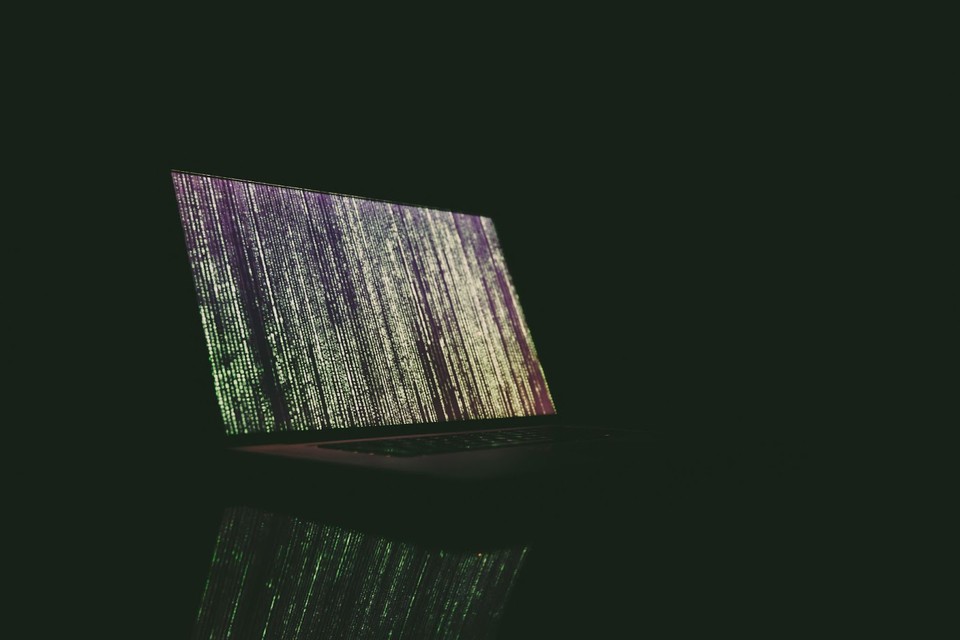 An Open Computer Against a Black Background Displays Lines of Code.