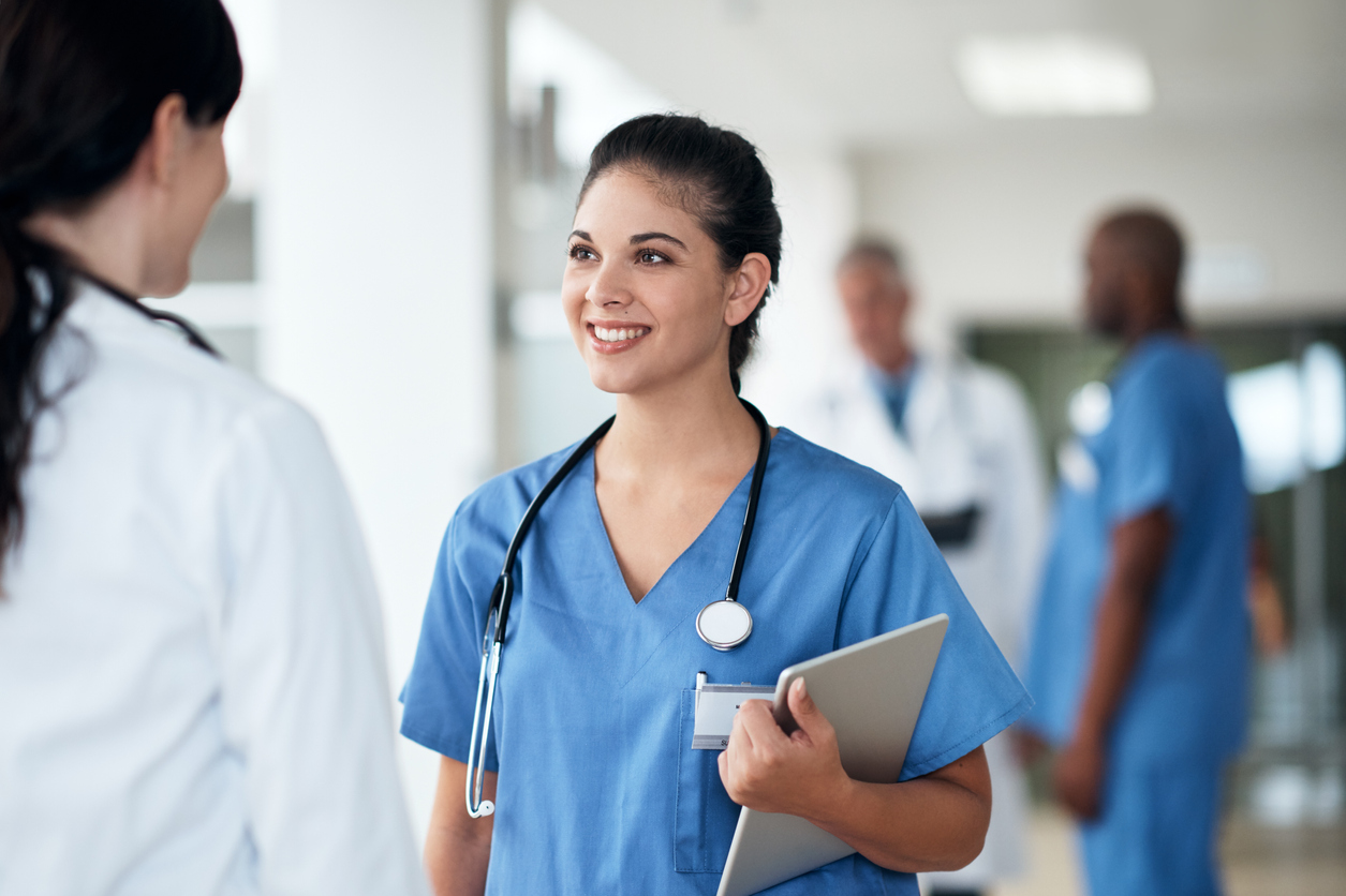 A nurse stands in a hallway in a medical facility and speaks with a doctor.