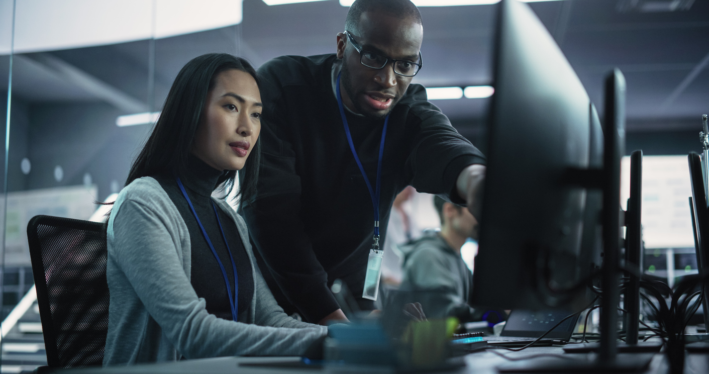 Cybersecurity compliance auditor working on a computer with a colleague.