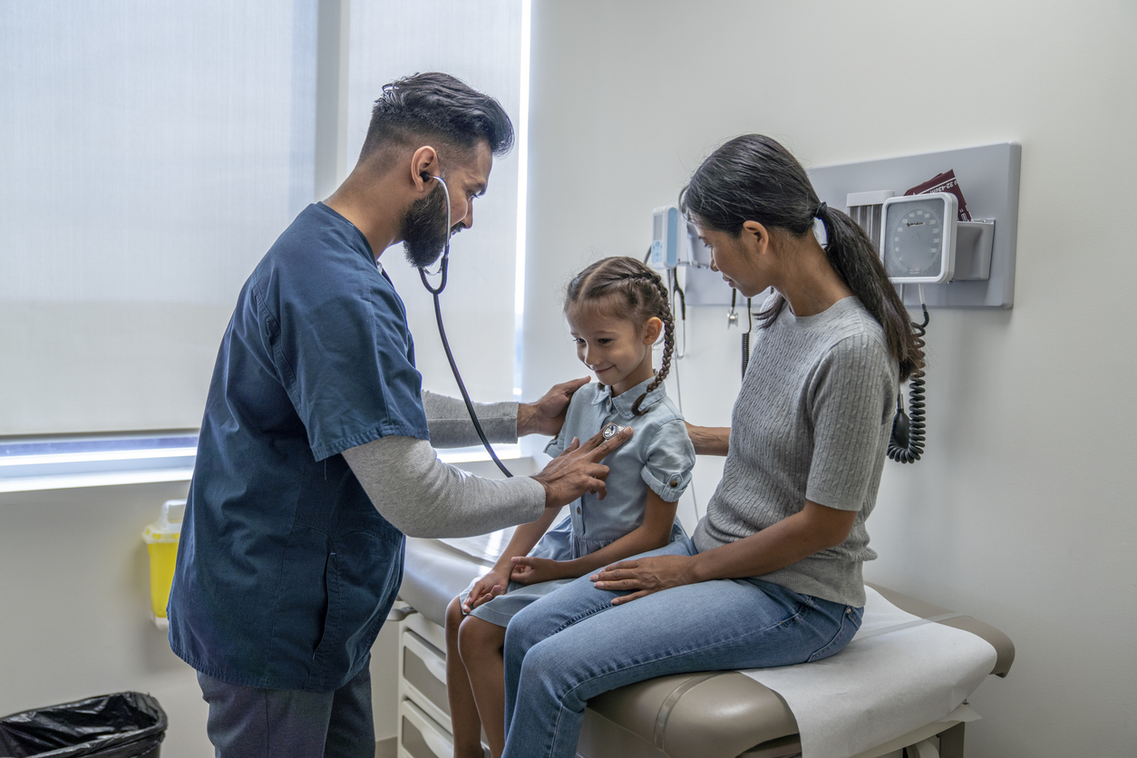 An FNP listens to a young patient’s heart with a stethoscope in an examination room.