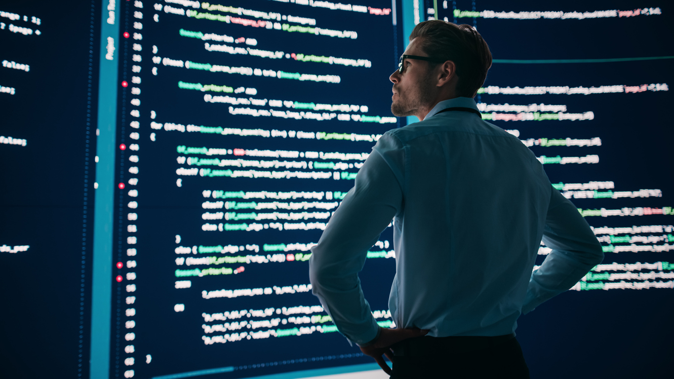 A Cybersecurity Professional Studies the Code Displayed on a Big Wall Screen.