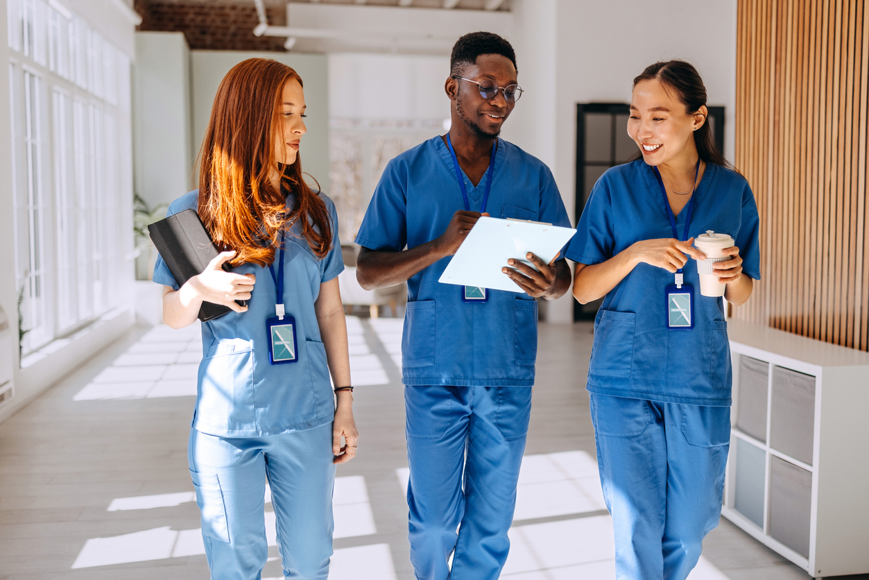 Three Nurses Wearing Scrubs Walk Down a Hospital Corridor..jpg