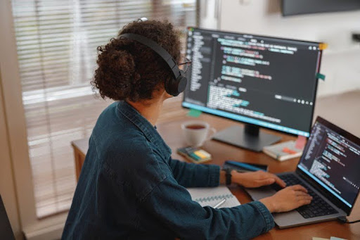 A programmer wearing headphones works on a monitor.