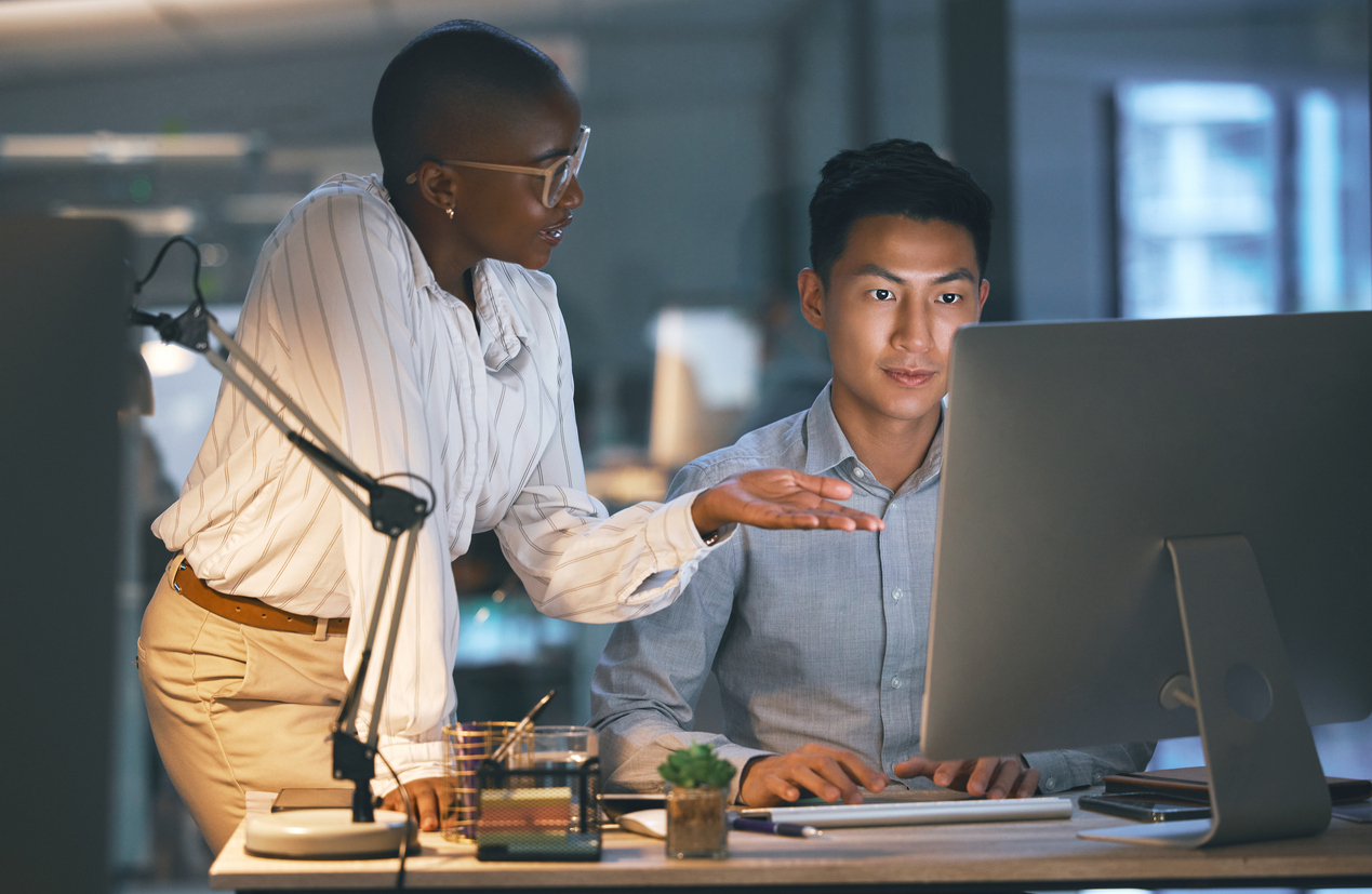 A Cybersecurity Professional Working With an Intern on a Computer in an Office.