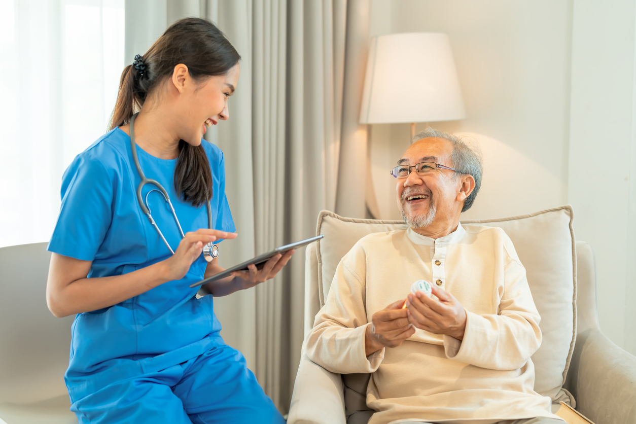 A Smiling Ag Acnp Holding a Tablet Consults With an Older Adult Patient.